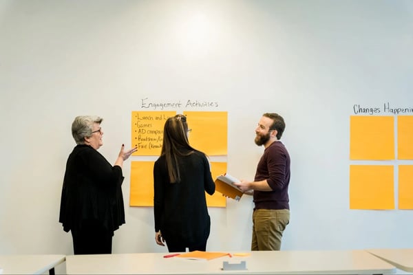 Three colleagues stand and talk while making list